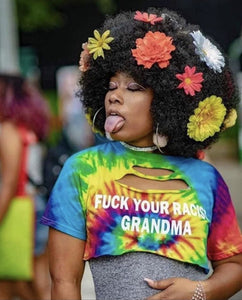 Woman with afro and flowers in her hair is sticking out her tongue and wearing a tie dye shirt that protests racism